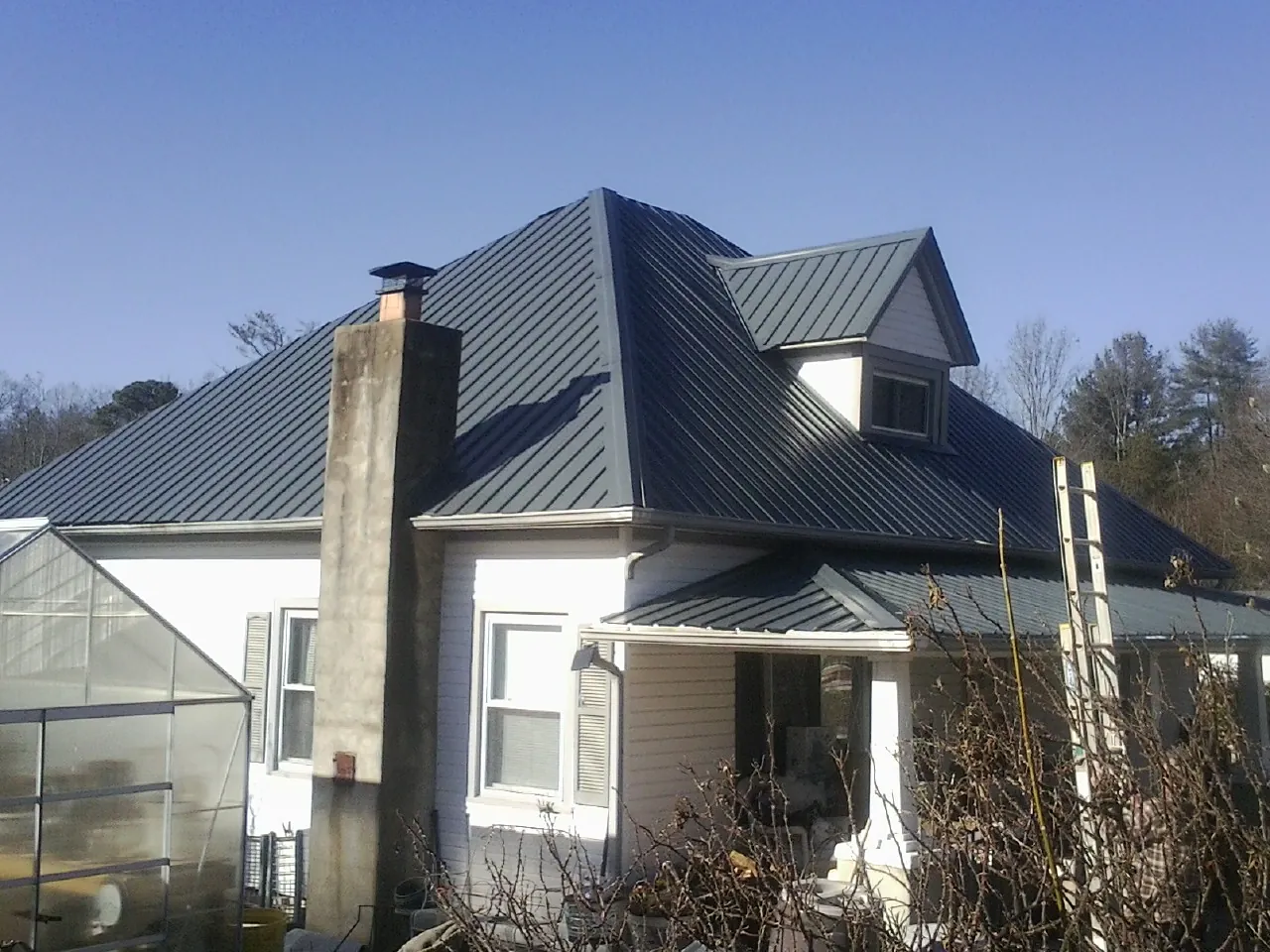 Dark blue standing seam metal roof on a white farmhouse with dormer — Slate & Tile Roof Repair by Roofing Brothers in Parrish